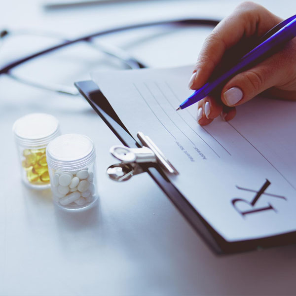 Close-up of a hand writing on an Rx prescription pad next to medication bottles.