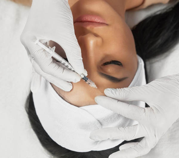 Professional aesthetician performing a facial injection on a relaxed female patient.