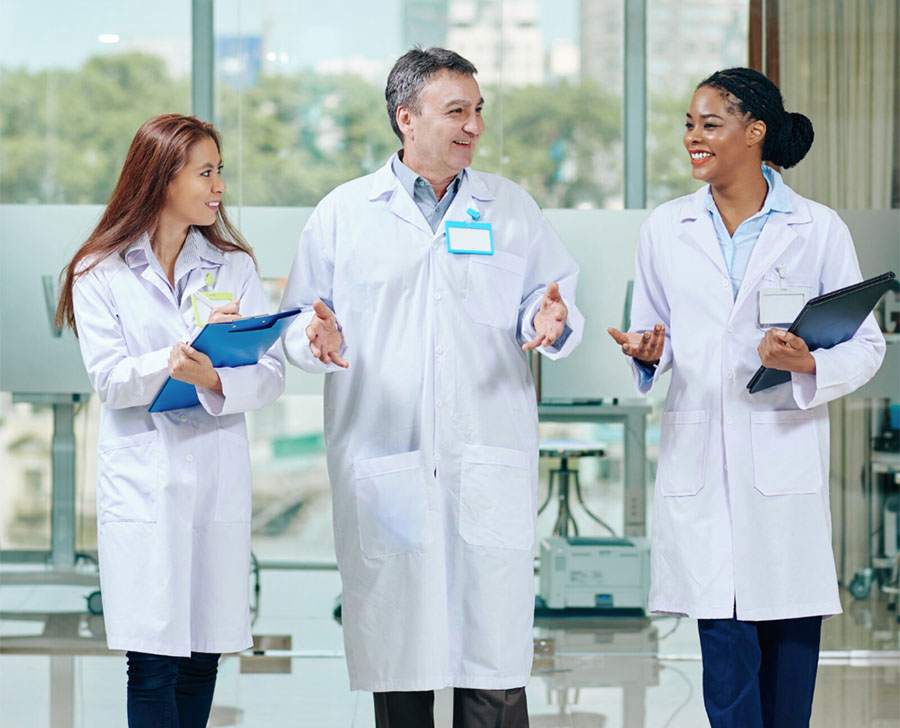 Three diverse medical professionals in white coats walking and talking in a modern hospital.