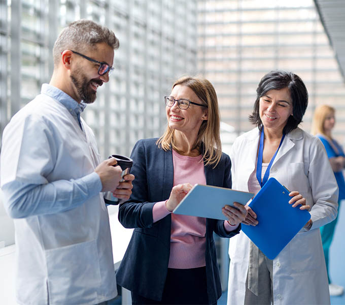 Medical professionals in white coats discussing information on a tablet with a colleague.