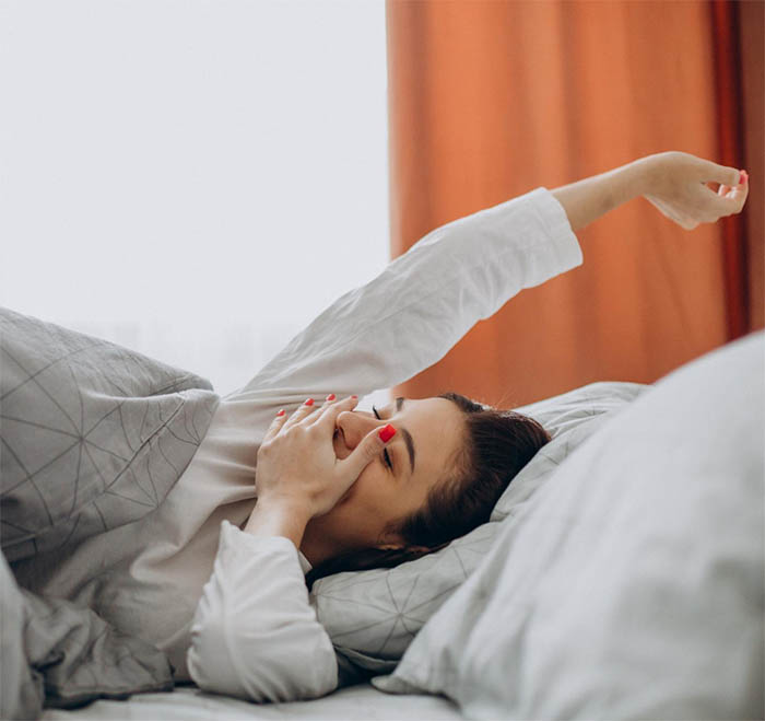 A young woman smiling and stretching in bed after a restful sleep, representing the benefits